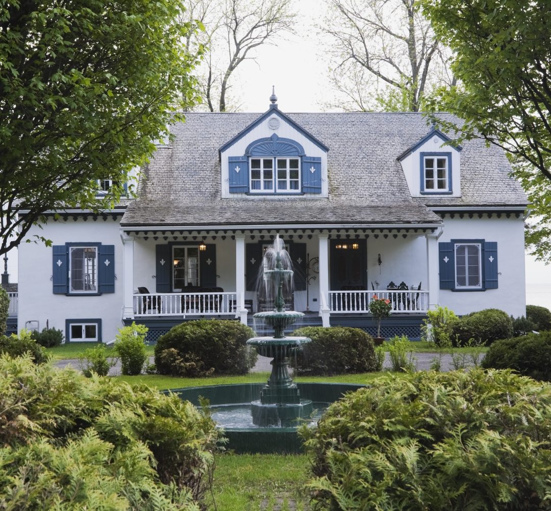 White with blue trim 1920s cottage style house facade with water fountain, Quebec, Canada